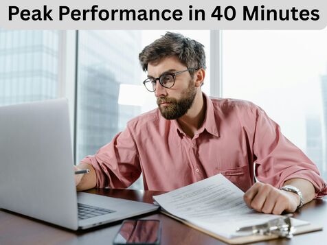 Professional businessman in salmon pink dress shirt working intensely at laptop with documents in modern office environment