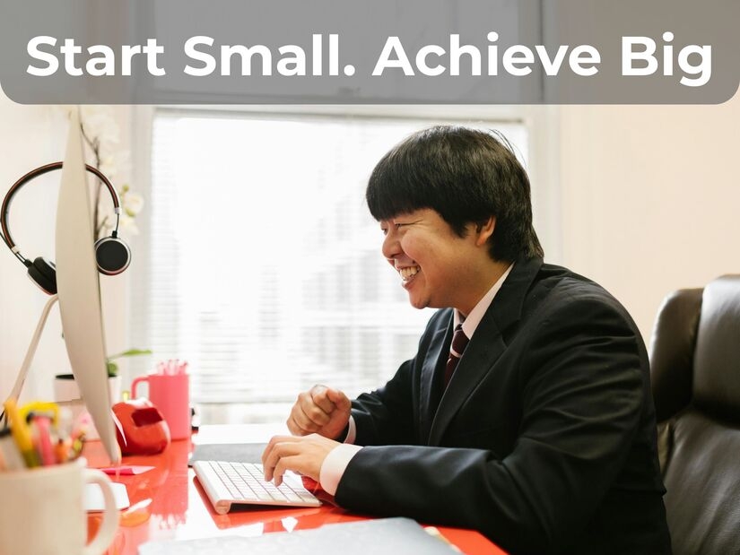 Professional smiling while working at desk with notebook demonstrating how starting small with 1 minute timer leads to big achievements