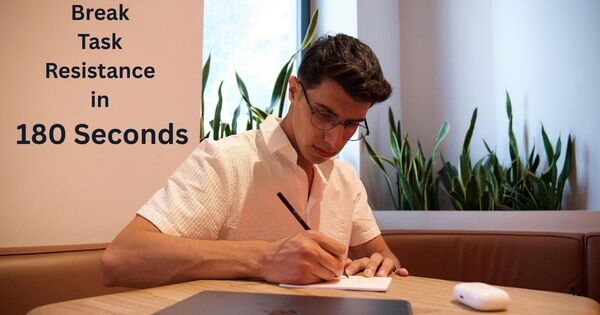A focused professional sitting at a wooden table writing notes next to a laptop to bypass procrastination.