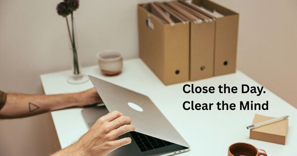 Hands closing a laptop at a desk with file boxes, representing the final 5 minute work shutdown ritual.